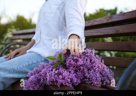 Jeune femme avec fleurs lilas sur banc en bois à l'extérieur Banque D'Images