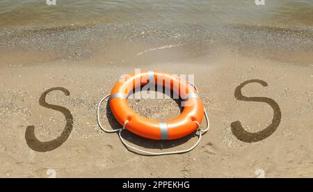 Message SOS manuscrit sur une plage de sable avec bouée de sauvetage près de la mer Banque D'Images