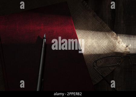 Un rayon de soleil dur tombe sur un vieux livre rouge. Sunbeam dans l'obscurité, sur un livre. Gros plan. Vieux livre rouge Banque D'Images