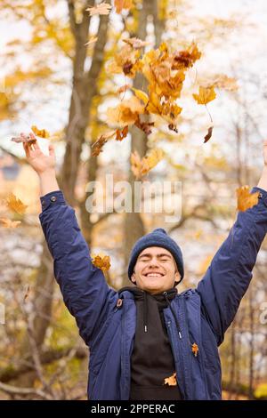 Un jeune homme souriant lance des feuilles d'automne Banque D'Images