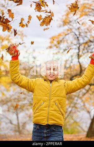 Jeune femme souriante jetant des feuilles d'automne Banque D'Images