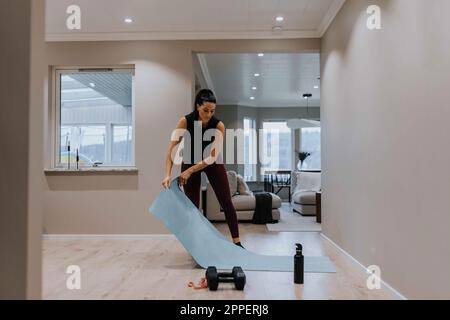 Femme mettant un tapis d'exercice sur le sol Banque D'Images