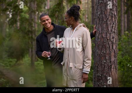 Couple souriant tenant des lunettes de vin dans la forêt Banque D'Images