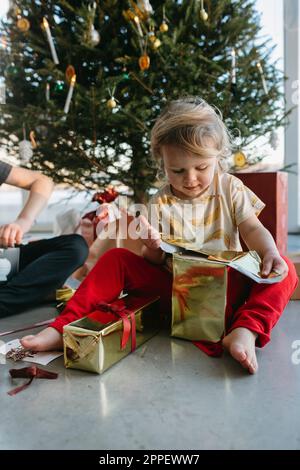 Fille ouvrant Noël présente sous l'arbre de Noël Banque D'Images