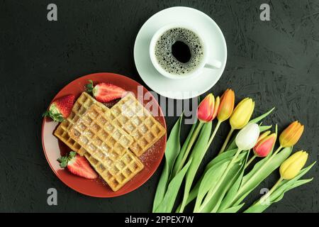 Tulipes fraîches et gaufres de fruits belges, vue de dessus. Petit déjeuner savoureux. Petit déjeuner pour un être cher. Gaufres faites maison sur une assiette. Arrière-plan avec espace de copie Banque D'Images