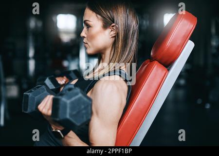 Le dur travail qui va dans l'aspect bien. une jeune femme s'entraîner avec des poids dans une salle de sport. Banque D'Images