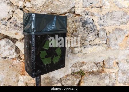 Poubelle noire avec symbole de recyclage vert dans la rue, espace de copie inclus Banque D'Images