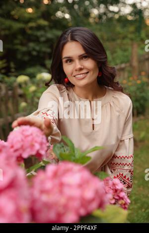 Belle femme portant une robe brodée dans un jardin fleuri. Vêtements nationaux ukrainiens Banque D'Images