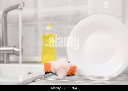 Panier de séchage avec plaque propre et éponge savonneuse dans une cuisine élégante Banque D'Images