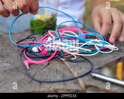 Les mains dénouent un nœud de quatre paires d'écouteurs intra-auriculaires filaires roses, bleus, blancs et noirs entremêlés dans un problème chaotique. Banque D'Images