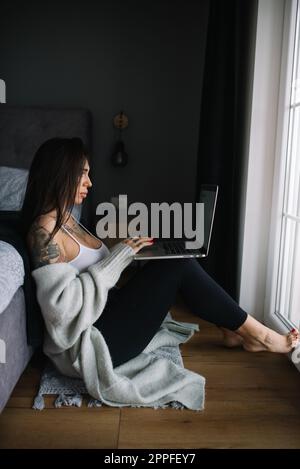 Femme tatouée travaillant sur un ordinateur portable assis sur le sol Banque D'Images