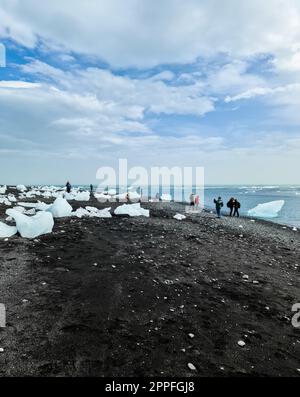 jokulsarlon, Islande - 23.juin 2022 : touristes à Diamond Beach en Islande avec des icebergs bleus fondant sur du sable noir et de la glace scintillant de lumière du soleil. Banque D'Images