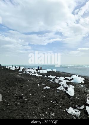 jokulsarlon, Islande - 23.juin 2022 : touristes à Diamond Beach en Islande avec des icebergs bleus fondant sur du sable noir et de la glace scintillant de lumière du soleil. Banque D'Images