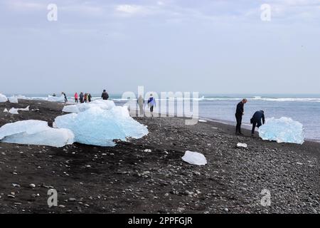 jokulsarlon, Islande - 23.juin 2022 : touristes à Diamond Beach en Islande avec des icebergs bleus fondant sur du sable noir et de la glace scintillant de lumière du soleil. Banque D'Images