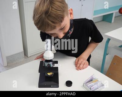 Sremska Mitrovica, Serbie, 15 mai 2021. Un garçon de 8 ans dans un T-shirt noir regarde avec un œil à travers un microscope. Cours de biologie. Le processus d'enseignement aux enfants. Cours scolaires Banque D'Images