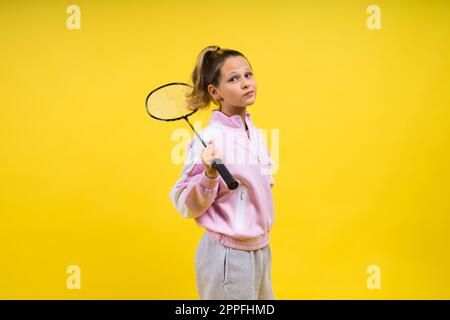 Photo studio pleine longueur d'une fille de dix ans tenant une raquette de badminton et isolée sur le jaune. Banque D'Images