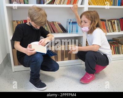 Sremska Mitrovica, Serbie, 15 mai 2021 enfants à la bibliothèque scolaire. Un garçon et une fille fouillent et feuillettent des livres dans le casier de la bibliothèque. Le garçon lit un livre très épais. Scolarisation. Les adolescents étudient Banque D'Images