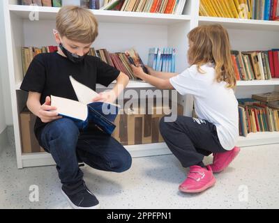 Sremska Mitrovica, Serbie, 15 mai 2021 enfants à la bibliothèque scolaire. Un garçon et une fille fouillent et feuillettent des livres dans le casier de la bibliothèque. Le garçon lit un livre très épais. Scolarisation. Les adolescents étudient Banque D'Images