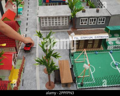 Un garçon en vêtements noirs tend la main à une table avec un modèle en papier - un modèle d'une ville ou d'un district. Affectation scolaire pour représenter votre rue. Leçon de travail ou projet à l'école. Banque D'Images