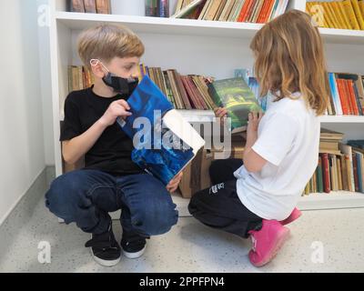 Sremska Mitrovica, Serbie, 15 mai 2021 enfants à la bibliothèque scolaire. Un garçon et une fille fouillent et feuillettent des livres dans le casier de la bibliothèque. Le garçon lit un livre très épais. Scolarisation. Les adolescents étudient Banque D'Images