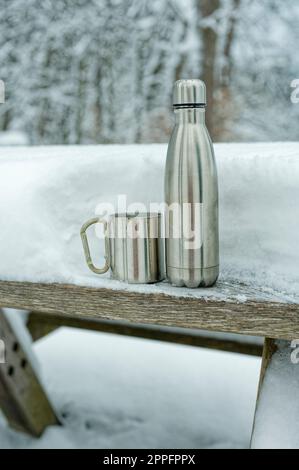 Thermos avec gobelet sur une table enneigée. Banque D'Images