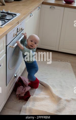 Petit garçon debout près du four dans la cuisine et regarde loin Banque D'Images