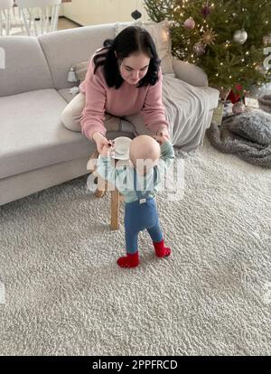 Une jeune mère tient un enfant debout près du canapé Banque D'Images