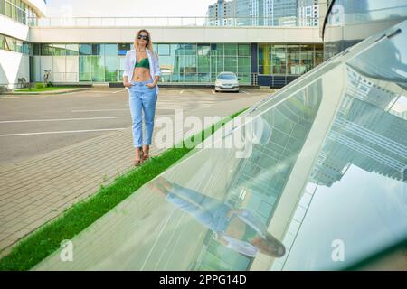 Jolie dame en jeans bleus et veste en cuir blanc près de l'immeuble de bureaux moderne Banque D'Images
