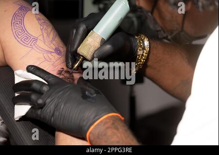 Vue rapprochée du processus de tatouage. Maître fait des lignes de contour avec sa machine de tatouage professionnel. Banque D'Images