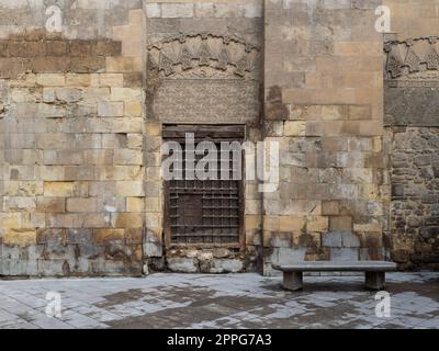 Fenêtre en bois avec grille en fer décorée sur un mur en briques de pierre et un banc de jardin en marbre Banque D'Images