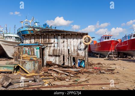 Shabby petit bâtiment en bois parmi lot de carton, et vieux navires rouillés dans la vieille usine de construction navale Banque D'Images