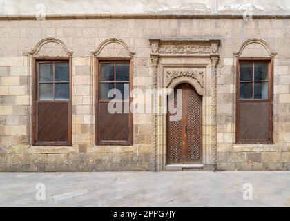 Vieux mur de briques décorées en pierre abandonnée avec porte en bois voûtée et trois fenêtres à volets Banque D'Images