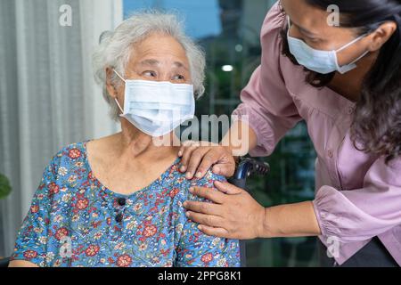 Aide-soignant asiatique senior ou âgée femme âgée assise sur un fauteuil roulant et portant un masque pour protéger l'infection Covid 19 coronavirus. Banque D'Images