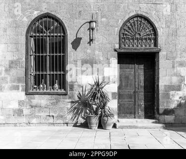 Mur en briques de pierre abandonnées noir et blanc avec porte en bois, fenêtre en fer forgé et lanterne Banque D'Images