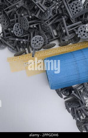 Ensemble d'éléments de construction pour l'isolation des murs. Des chevilles en plastique, un rouleau de maille pour l'isolation des façades et un profil d'angle avec une grille se trouvent sur la surface en mousse de polystyrène Banque D'Images