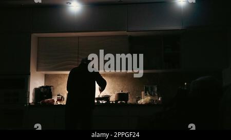 Homme cuisinant avec des lampes torches sur une cuisine pendant la panne de courant en ukraine. Concept d'interdiction en Ukraine. Homme cuisant dans l'obscurité avec des lumières torches autour Banque D'Images