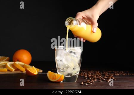 Femme versant du jus d'orange dans le verre avec des glaçons à table en bois, gros plan Banque D'Images