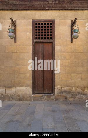 Porte fermée en bois et lanternes de rue en verre arabe accrochées à un poteau en bois dans un vieux mur de briques en pierre Banque D'Images