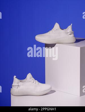 Paire de sneakers tendance pour femme sur fond bleu, avec une passerelle blanche. Banque D'Images