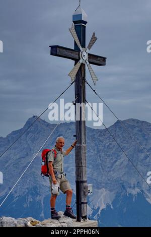 Europe, Autriche, Tyrol, Alpes d'Ammergauer, montagne de Daniel, croix de sommet, randonneur, sac à dos, massif de Zugspitz (arrière-plan) Banque D'Images