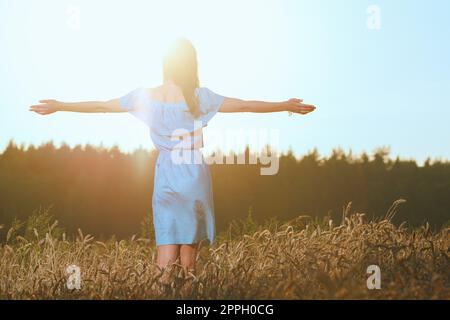 Belle jeune fille en champ de blé au coucher du soleil. Fille en robe bleue occasionnels bénéficiant d soirée ensoleillée Banque D'Images