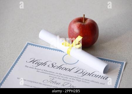 Un diplôme d'études secondaires repose sur la table avec un petit rouleau et une pomme rouge. Documents éducatifs Banque D'Images