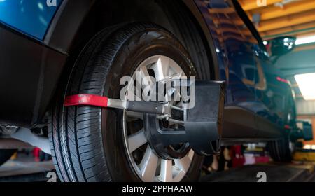 L'équipement de réglage de la géométrie des roues adhère au pneu de la roue de voiture dans l'atelier de réparation automobile. Alignement automatique des roues dans l'atelier de la station-service. Equilibre des roues de la voiture. Réglage de la suspension. Véhicule à l'intérieur de l'atelier de garage. Banque D'Images