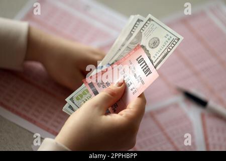 Une jeune femme tient le billet de loterie avec une rangée complète de chiffres et de billets de dollar sur le fond des feuilles vierges de loterie Banque D'Images