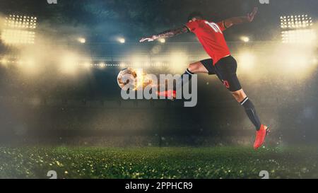 Scène de football la nuit, match avec un joueur dans un uniforme rouge donnant un coup de pied à une balle ardente avec de la puissance Banque D'Images