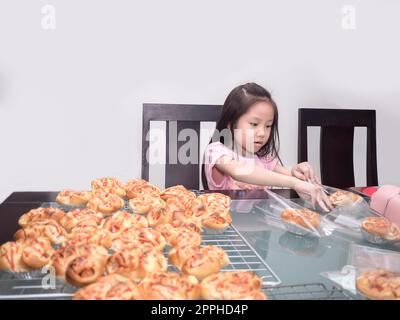 Adorable petite fille emballage séparé saucisse de porc cuite avec pain de mayonnaise, cuisine domestique, enfant aidant ses parents Banque D'Images