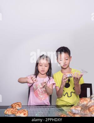 Adorable enfant fille et garçon emballage séparé saucisse de porc cuite avec pain de mayonnaise, cuisine domestique, enfant aidant ses parents Banque D'Images