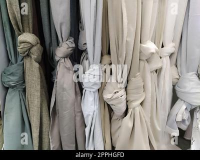 Rideau et tissu pour draperie et décoration intérieure. Des échantillons de tissus gris et blancs dans le magasin sont suspendus verticalement et noués en nœuds. Rideaux dans la vitrine. Banque D'Images