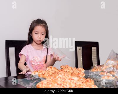 Adorable petite fille emballage séparé saucisse de porc cuite avec pain de mayonnaise, cuisine domestique, enfant aidant ses parents Banque D'Images