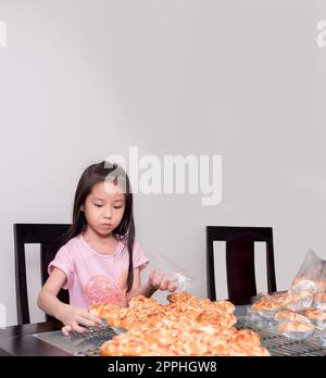 Adorable petite fille emballage séparé saucisse de porc cuite avec pain de mayonnaise, cuisine domestique, enfant aidant ses parents Banque D'Images